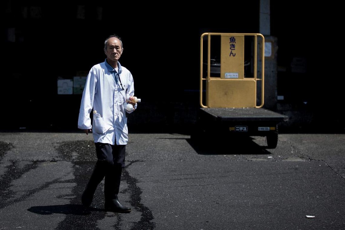 Portrait of Japanese worker at Tsukiji Fish market in Tokyo Japan next to yellow trolley. Photography by Darren Gill
