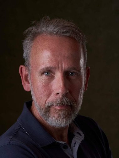 bearded man looking at the camera with a dark background. Headshot photographer - Clive Allcorn
