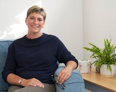 Image of smiling woman with blonde hair sitting in an armchair with pot plant nearby. Headshot Photography by Clive Allcorn