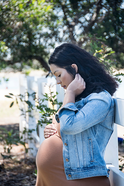 Profile portrait of a young pregnant woman looking down and holding her belly