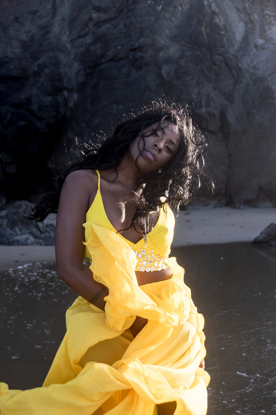 Portrait of a young black woman wearing a bright yellow dress on the beach