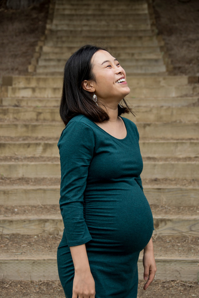 Portrait of a young asian pregnant woman wearing a tight green dress in front of stairs 