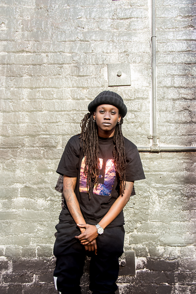 Portrait of a young black gay woman in all black against a wall