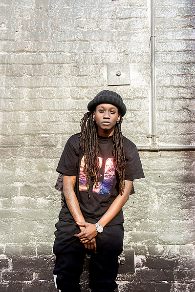 Portrait of a young black gay woman in all black against a wall