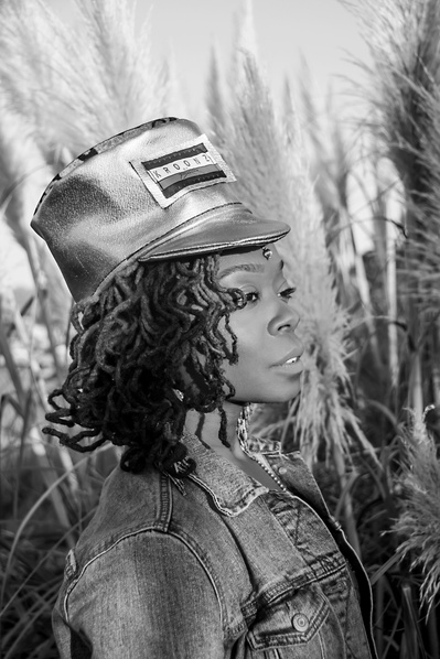 Black and white portrait of a young black woman wearing a tall hat in a field