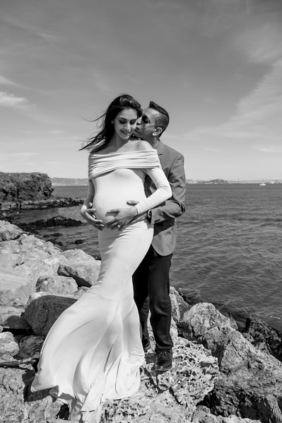 Pregnant woman and her partner standing on rocks at the side of the ocean