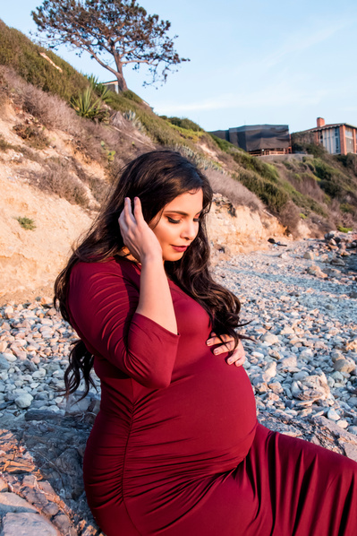 Pregnant woman wearing tight red dress sitting by the beach