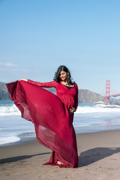 Young pregnant woman wearing a red dress by the ocean shore with the golden gate bridge in the background