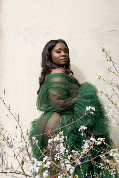 Portrait of a young black woman wearing a mesh green dress with flowers in the foreground