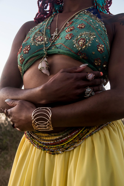 Torso of a young black woman wearing vibrant clothes, an amethyst necklace and many waist beads