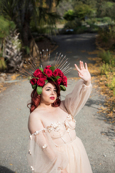 Portrait of a young Mexican woman wering a red rose crown and flowy dress in a garden
