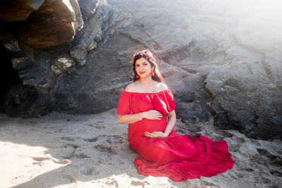 Pregnant Indian woman sitting on sand wearing a red dress