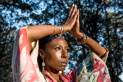 Portrait of a young black woman with prayer hands wearing bangles and cowry earrings