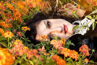 Young white woman with dark hair laying in a field of orange flowers