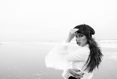 Black and white portrait of a young woman wearing a beret and white flowy top on the beach