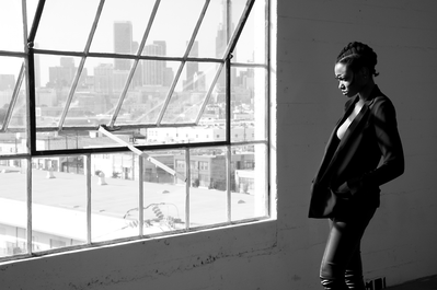 Black and white portrait of a young black woman wearing all black looking out a studio window