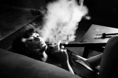Black and white portrait of a young woman laying down smoking hookah 