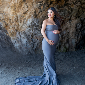 A maternity shoot in front of a beach cave wearing gorgeous bodycon dress