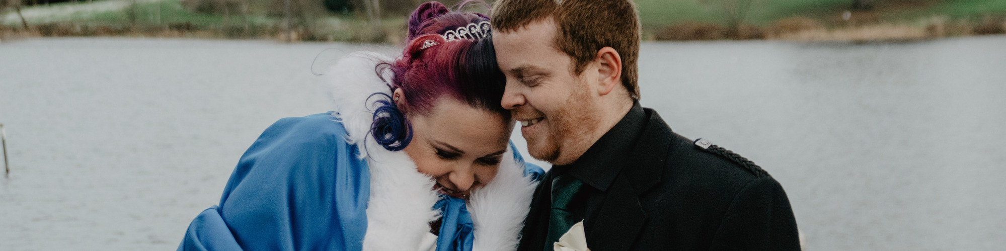 Bride and groom on winter day standing on dock in front of lake.