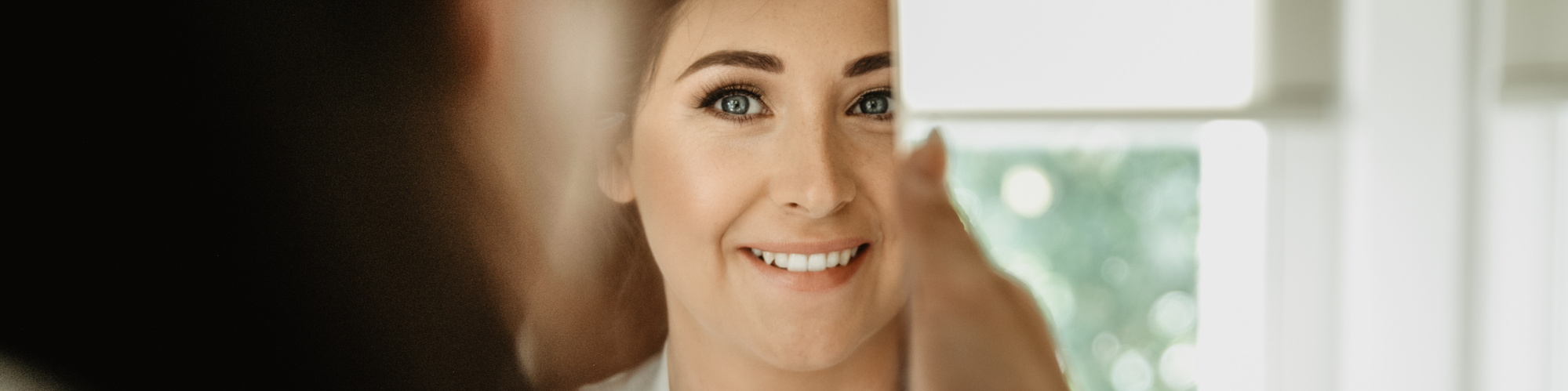 bride looking into her own reflection during bridal prep in front of window.
