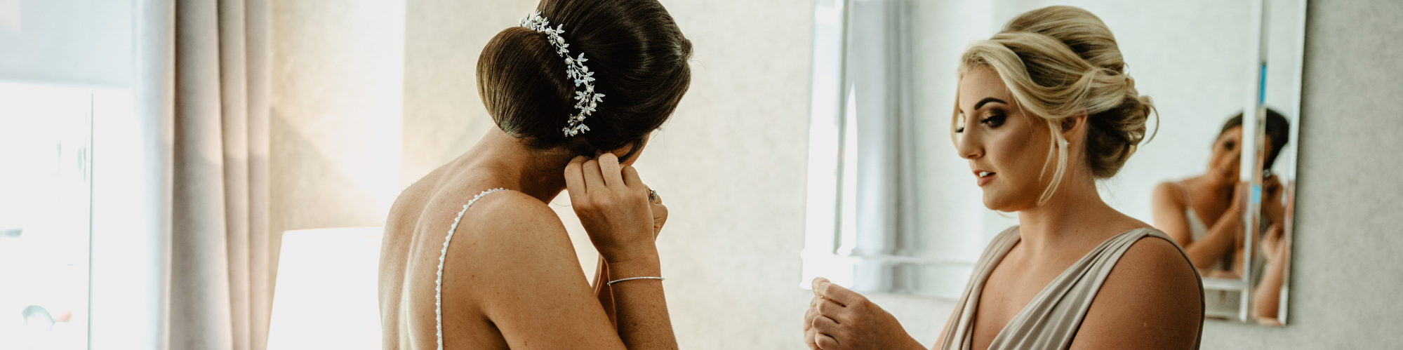 bride looking at herself in mirror putting on jewellery before ceremony