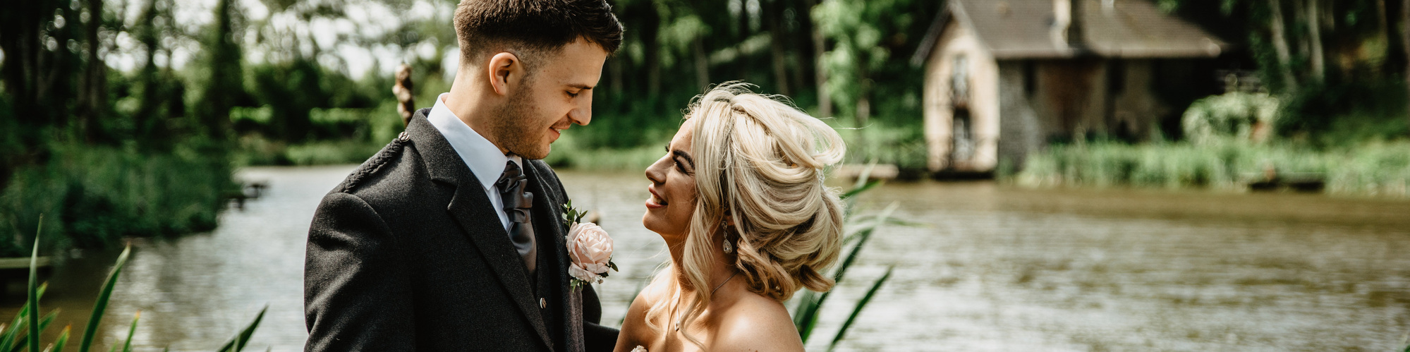Bride and groom looking into each others eyes in front of lake and boathouse.