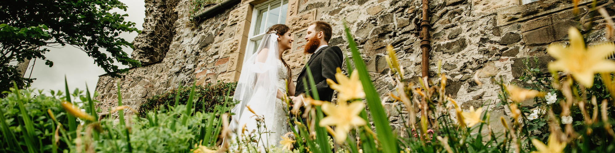 bride and groom standing in front of castle with yellow daffodils 