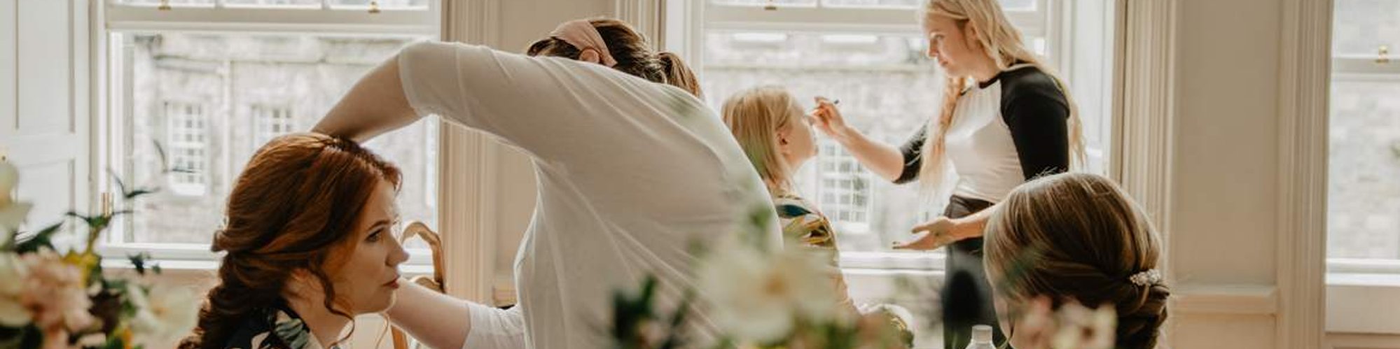 bride and bridesmaids getting ready with hairdressers and makeup artists before ceremony.