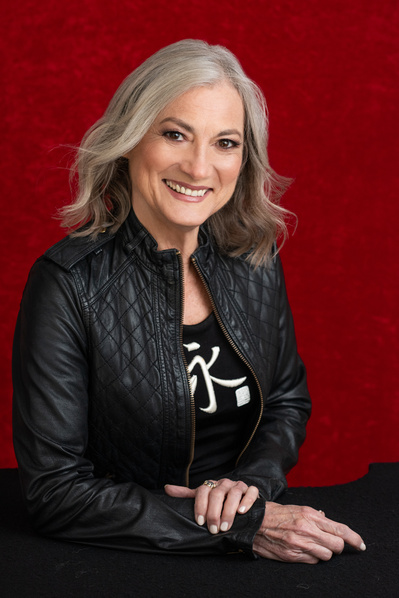 Headshot of pretty older woman seated wearing a black leather jacket