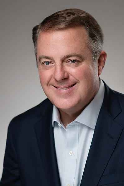 Attractive male executive studio headshot in dark suit smiling.