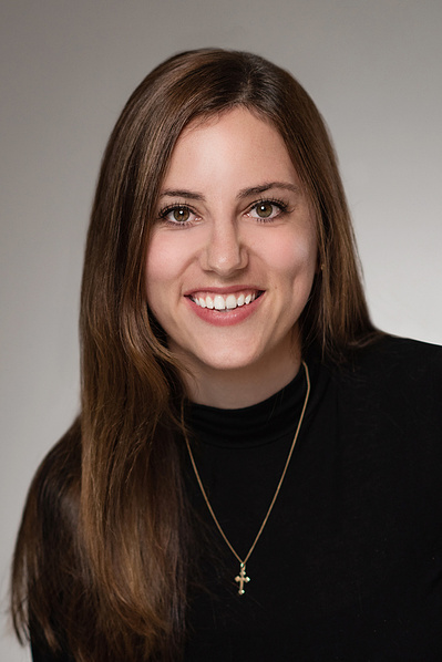 Headshot of dark haired executive female with dark top and cross necklace