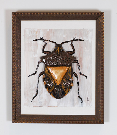Framed dark colored ceramic beetle.