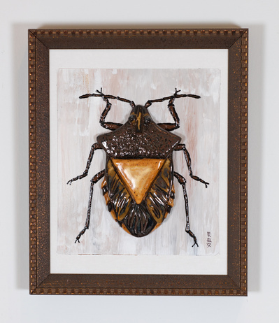 Framed dark colored ceramic beetle.