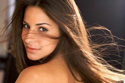 Beautiful young brunette woman, studio portrait with hair blowing across face
