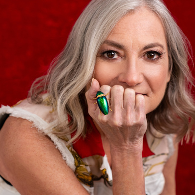 Attractive older female artist headshot with green Bug ring in front of face