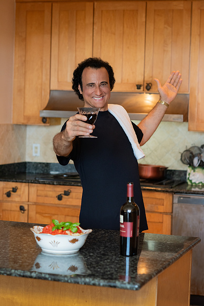 Male opera singer in kitchen with pasta bowl on counter and wine glass in hand