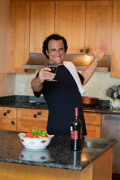 Male opera singer in kitchen with pasta bowl on counter and wine glass in hand