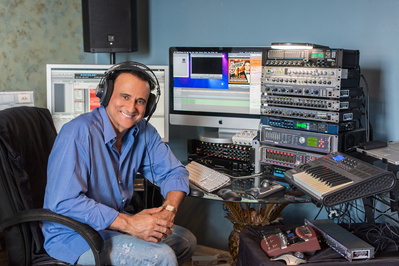 Seated male opera singer in front of his technical musical gear with headphones on.