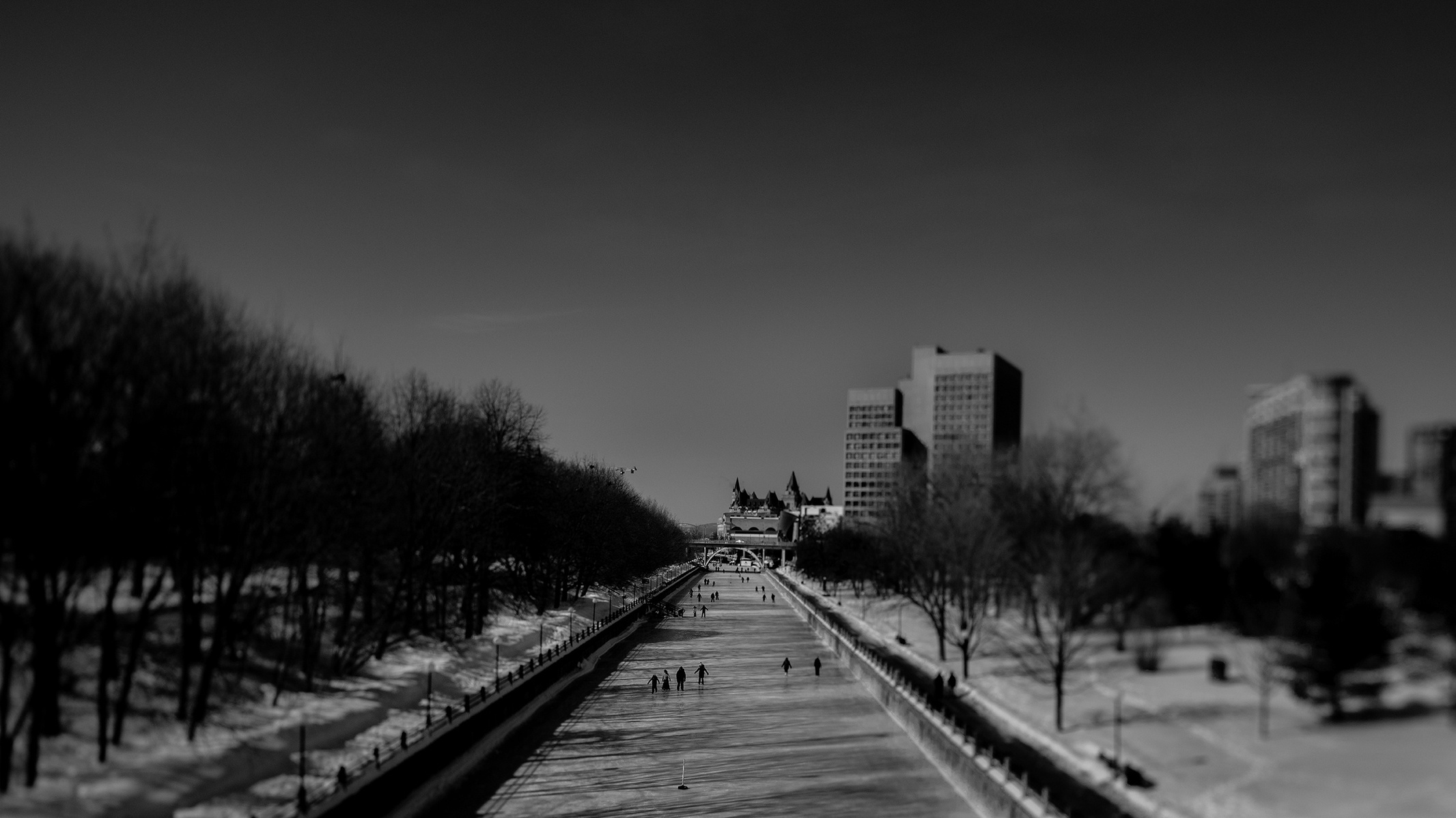 Rideau Canal skaters in black and white with Chateau Laurier in background from Tappers Bridge