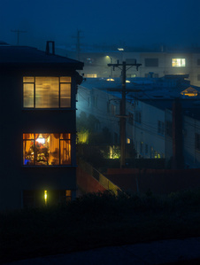 San Francisco houses, veiled in fog, are lit from within, with some interiors more visible than others.