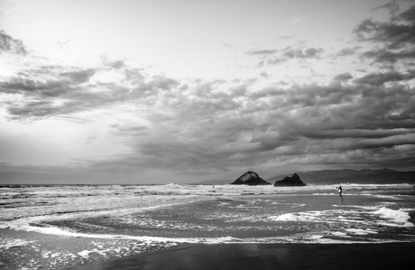 A black and white photo of two rocks off the coast of Ocean Beach on a cloudy dramatic day at high tide.