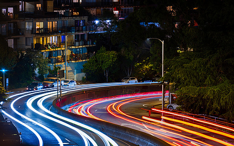 A long exposure shot of traffic heading down upper Market Street in San Francisco toward The Castro with lit-up apartments in the background.