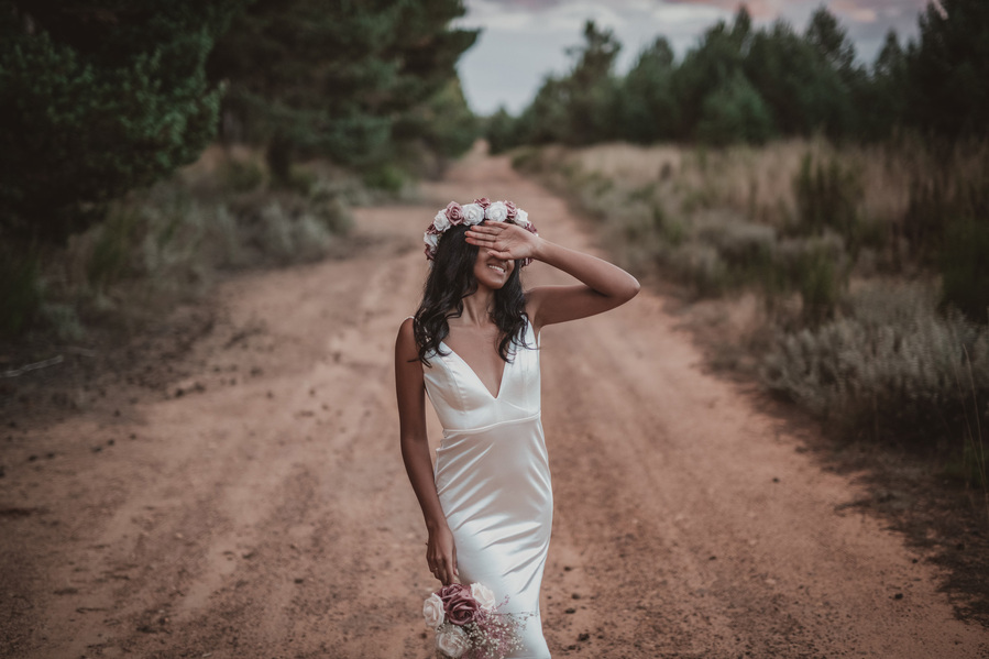 mujer vestida de novia se tapa la cara con la mano en un camino