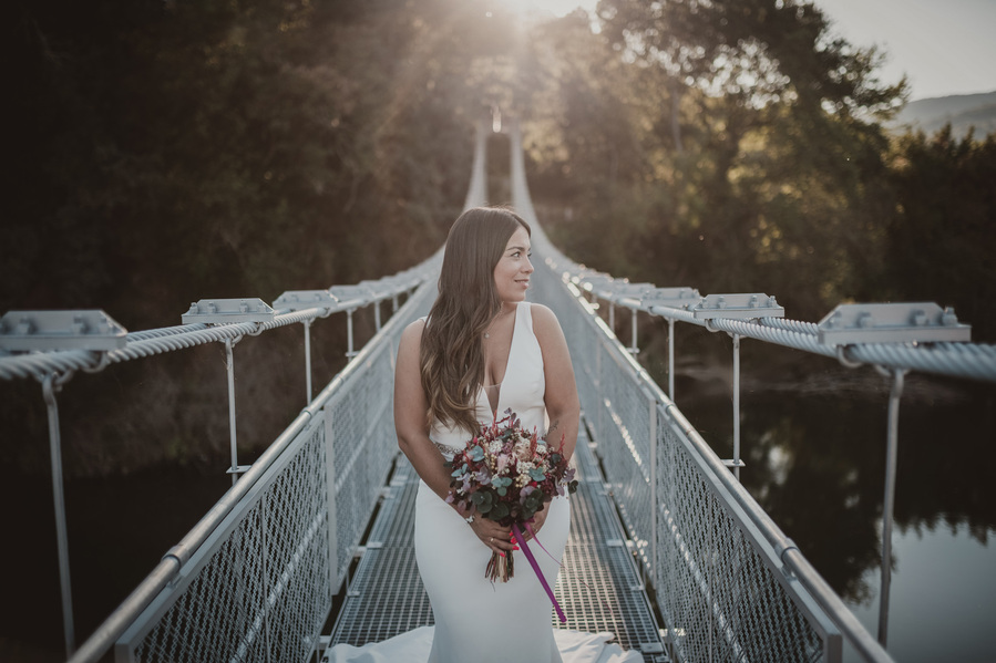 mujer vestida de novia con un ramo en las manos en un puente colgante