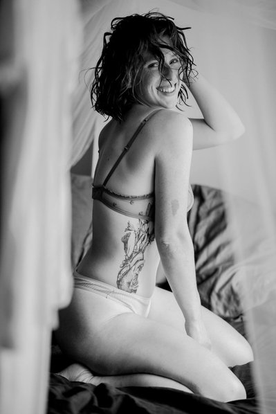 A curly hair woman with a tattoo, wearing  lingerie during a boudoir photo session advertising underwear 