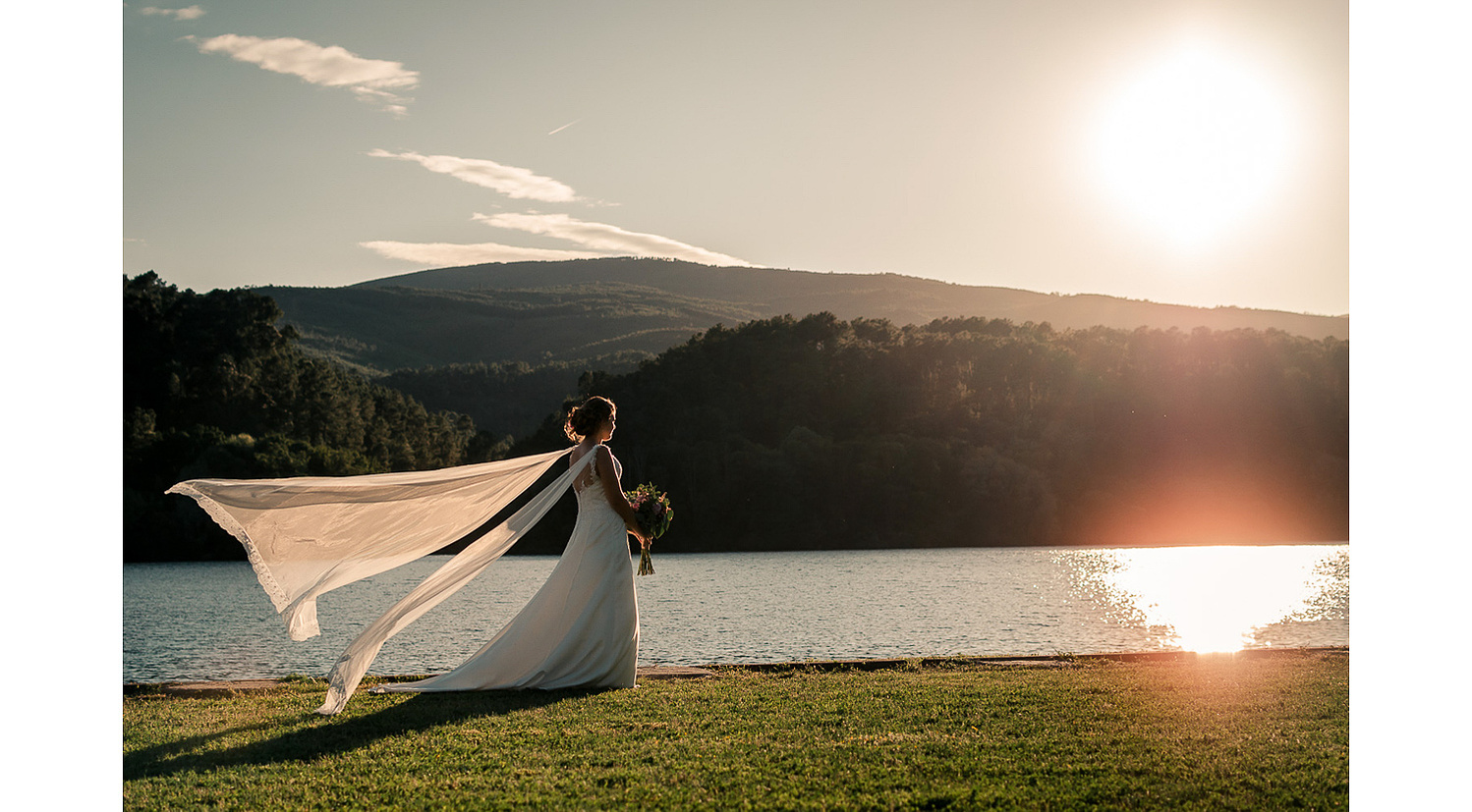 Fotografía espectacular de vestido de novia durante la puesta de sol con un lago de fondo, el velo al vuelo en Arnoia