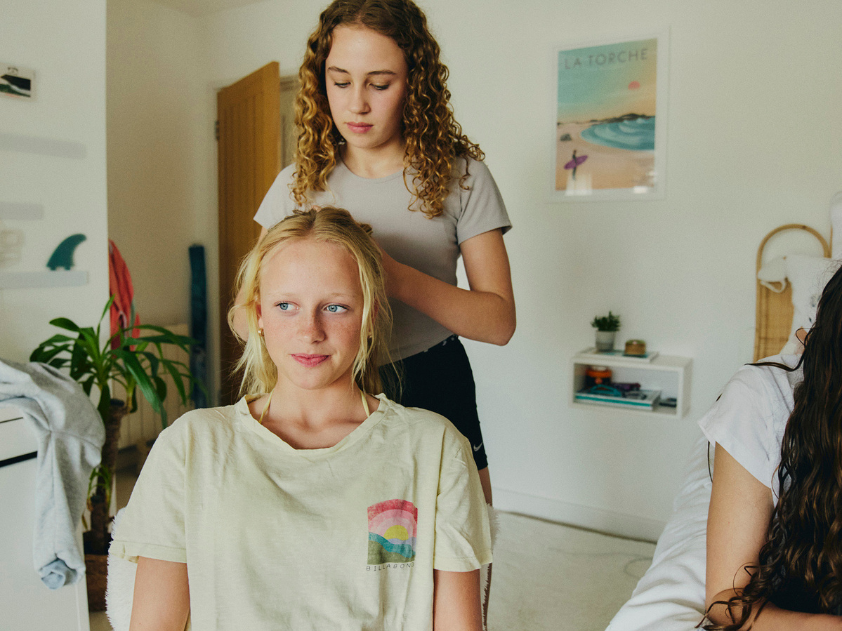 Two girls plaiting hair at a sleepover in a bedroom