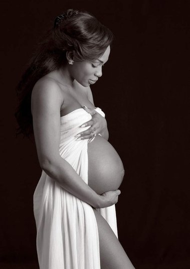 Maternity photo in professional photography studio with black background women in white dress with pregnant bump exposed