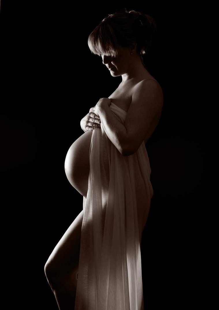 Natural  maternity portrait photo in professional photography studio using black background, side view of pregnant woman bump with draping fabric silhouette
