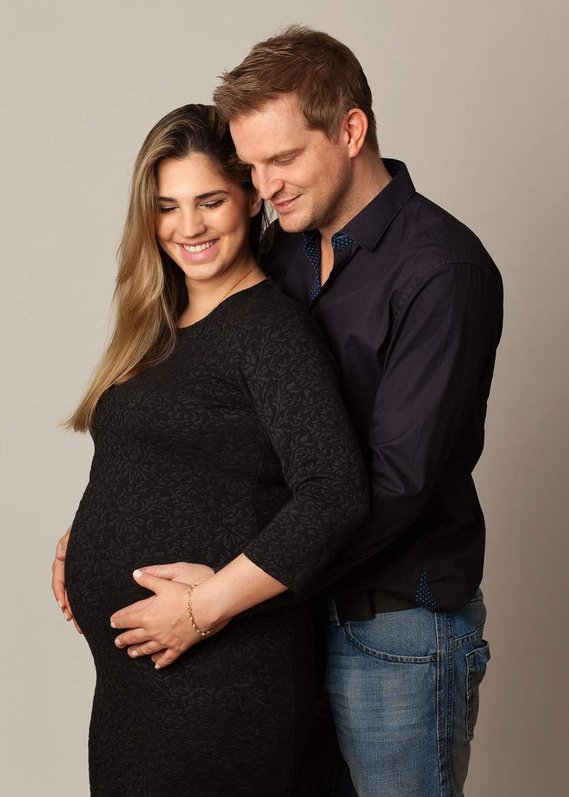 Natural  maternity portrait photo of a young couple standing close together in professional photography studio with father and mothers hands placed together on her pregnant bump